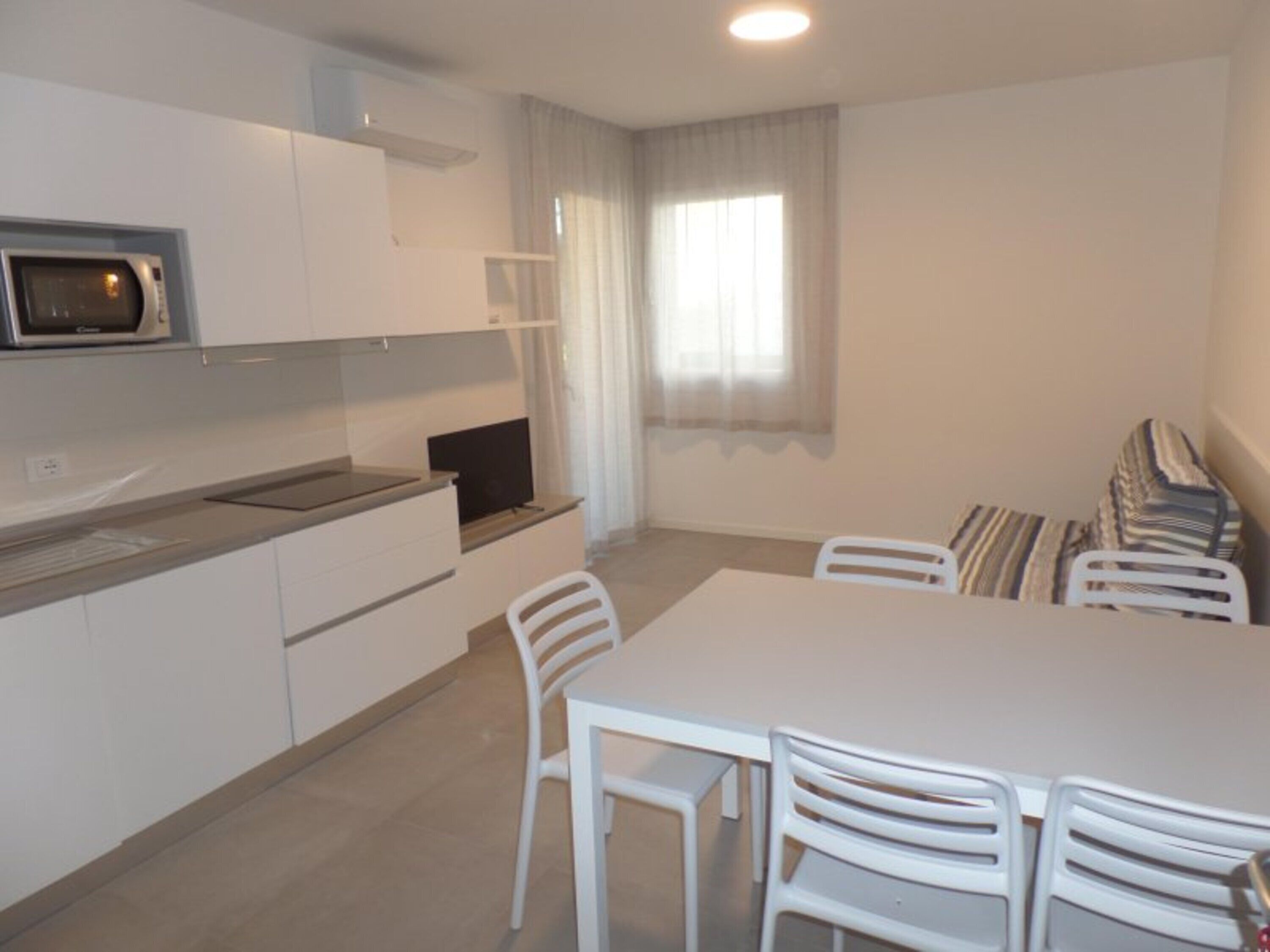 Una cocina compacta con microondas, una mesa de comedor con sillas y un ventanal con cortinas.