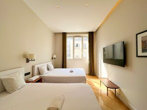 Ein Hotelzimmer mit zwei Betten, einem Fernseher, einem Fenster mit Vorhängen und Holzboden.