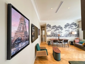 Ein Hotelzimmer mit Essbereich, einem großen gerahmten Bild des Eiffelturms, einer Wandmalerei von Bäumen und einem modernen Design.