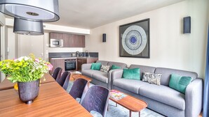 Un salon moderne avec un canapé gris, une table à manger avec des chaises, un coin cuisine et un grand tableau abstrait accroché au mur.