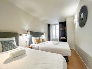 Ein Hotelzimmer mit zwei Betten, einem Fenster, einem Spiegel und einem kleinen Tisch.