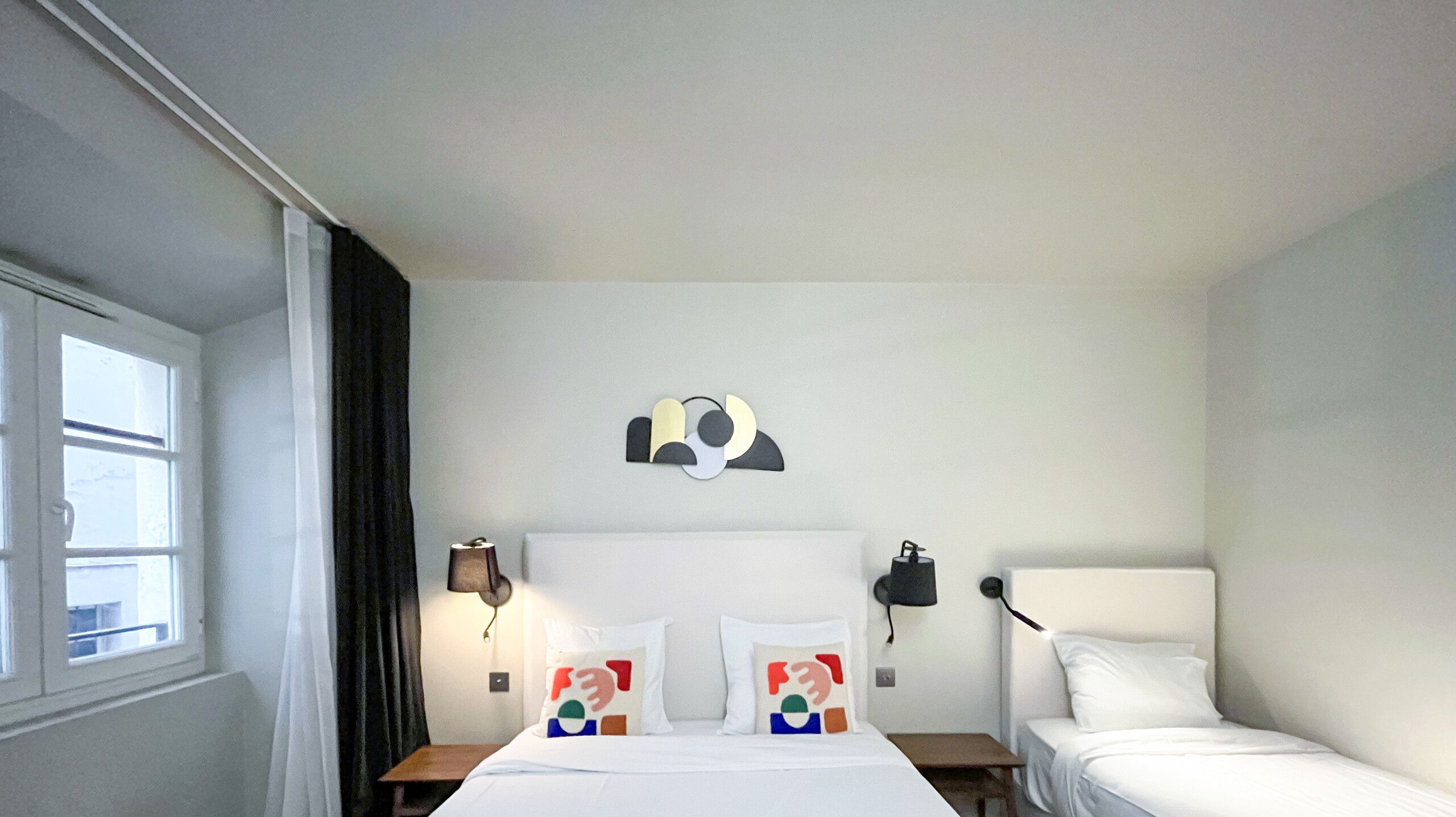 Een hotelkamer met een bed, twee nachtkastjes, een kunstwerk aan de muur en een raam met gordijnen.
