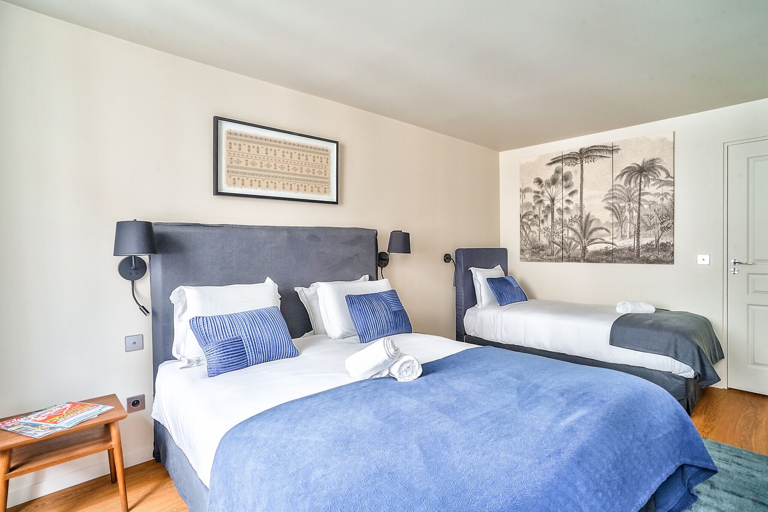A bedroom with two beds, a nightstand, a framed picture, and a door.