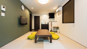 Una sala de estar moderna con una mesa de madera, sillones de peluche amarillos, un televisor de pantalla plana y una cocina al fondo.