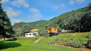 A house with a balcony, a white building, and a hill with trees. - Mountain Front Hut For 2 Rare Birds, Bikes, Nature (Kaeng Krachan)