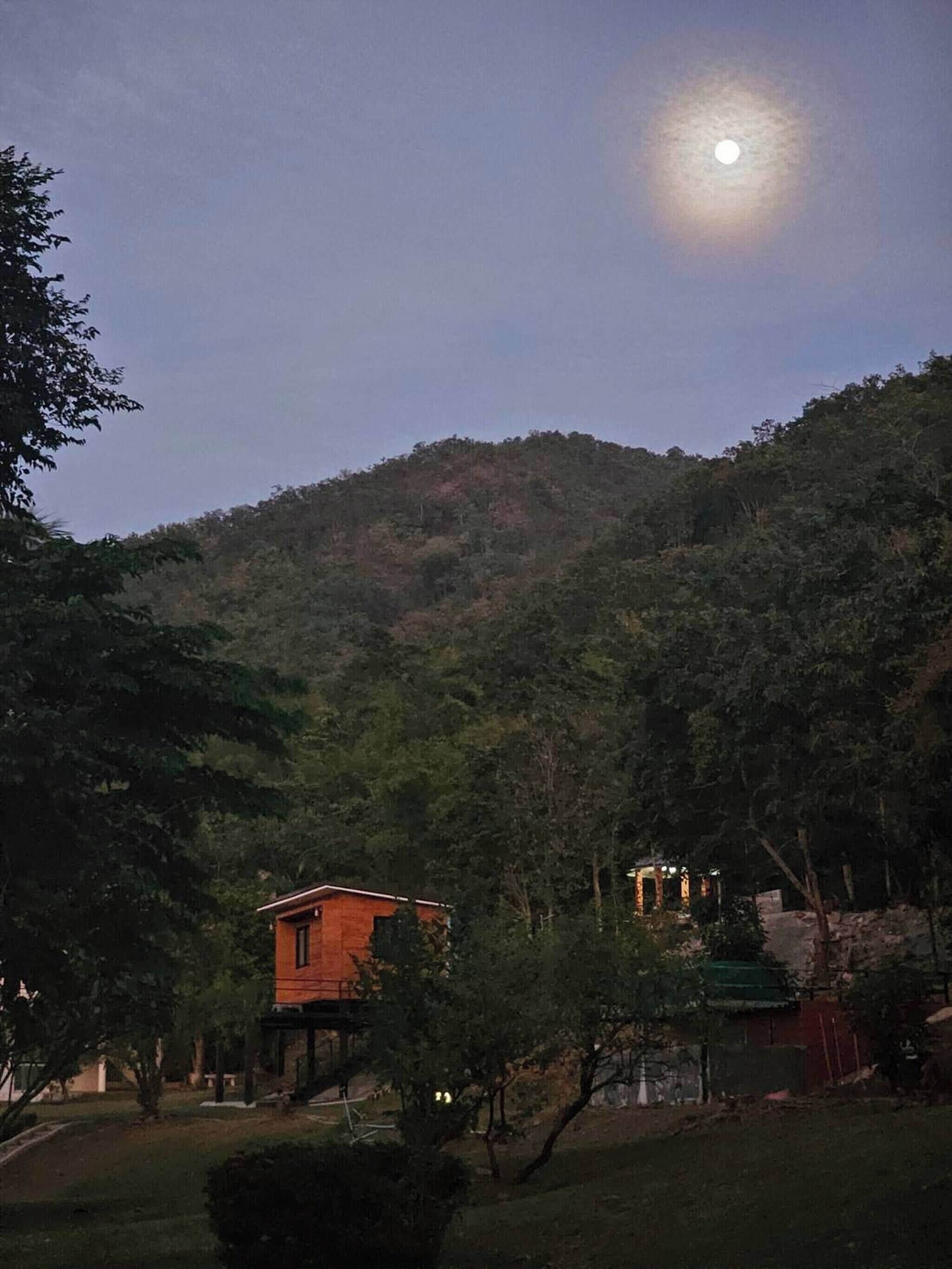 Una casa con porche, rodeada de árboles y una colina.