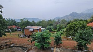 A black dog lying on a tiled surface, a wooden building, and a pond in a rural setting. - Mountain Front Hut For 2 Rare Birds, Bikes, Nature (Kaeng Krachan)