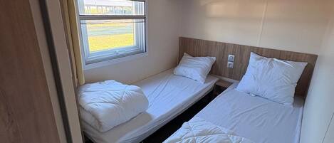 Un dormitorio compacto con dos camas individuales, una ventana con vistas y un cabecero de madera.