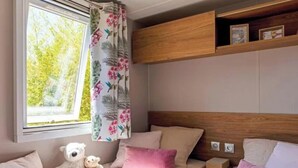 A bedroom with a bed, a window with curtains, a shelf with pictures, and a teddy bear. - Pocket" mobile home in the heart of the pony club (Hostens)