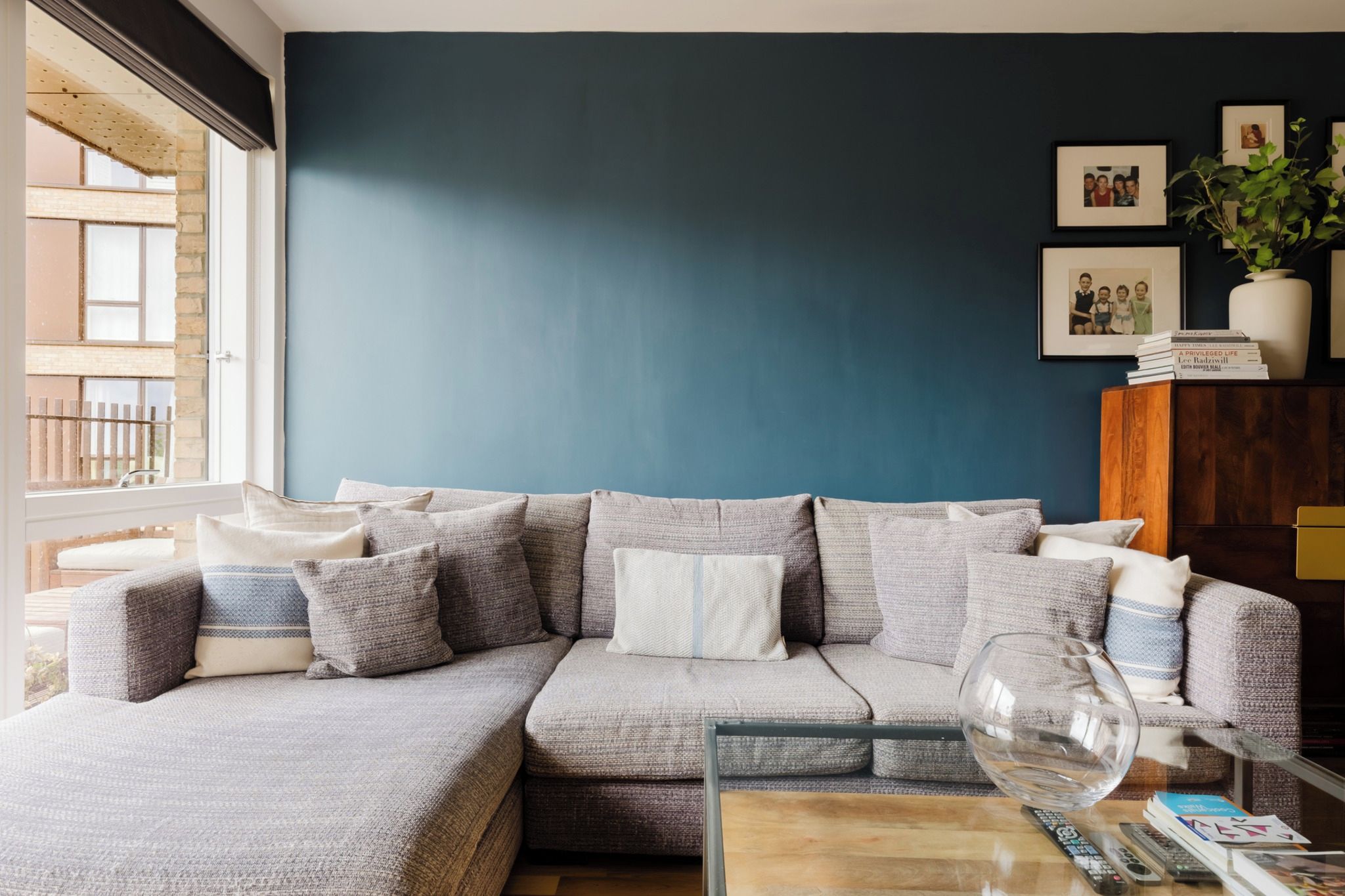 A living room with a sectional sofa, a glass coffee table, and a bookshelf with books and a vase.