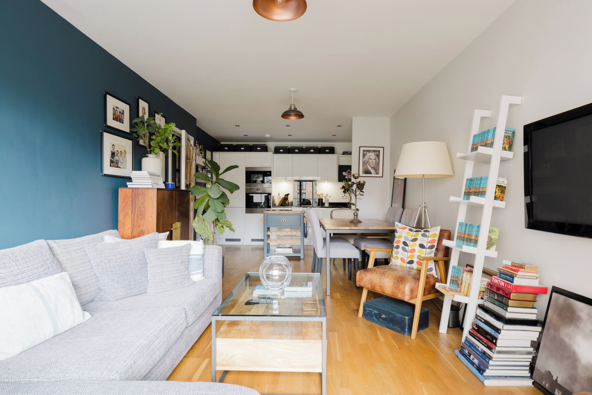 A modern living room with a sofa, coffee table, and a dining area with chairs. There is a kitchen in the background with cabinets and appliances.