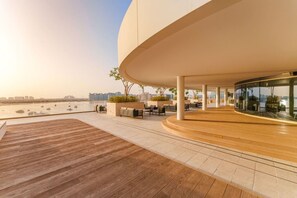 Ein modernes Gebäude mit geschwungener Außenfassade, Sitzgelegenheiten im Freien und Blick auf das Wasser.