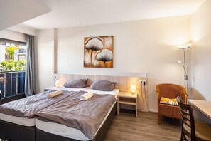 A hotel room with a bed, bedside tables, a chair, a desk, and a painting on the wall.