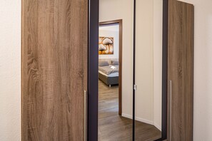 A room with a wooden wardrobe, a bed with a gray mattress, and a painting on the wall.