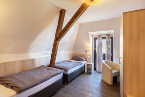 A small, modern bedroom with two beds, a wooden ceiling beam, a chair, and a window with curtains.
