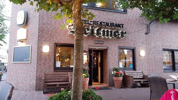 A brick building with a sign reading 'RESTAURANT Seittimer.' There are outdoor seating areas with benches and potted plants.