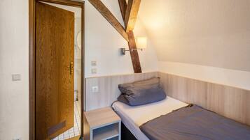 Ein Schlafzimmer mit Holztür, einem Bett mit grauer Matratze, einem kleinen Nachttisch und einer Wandleuchte.