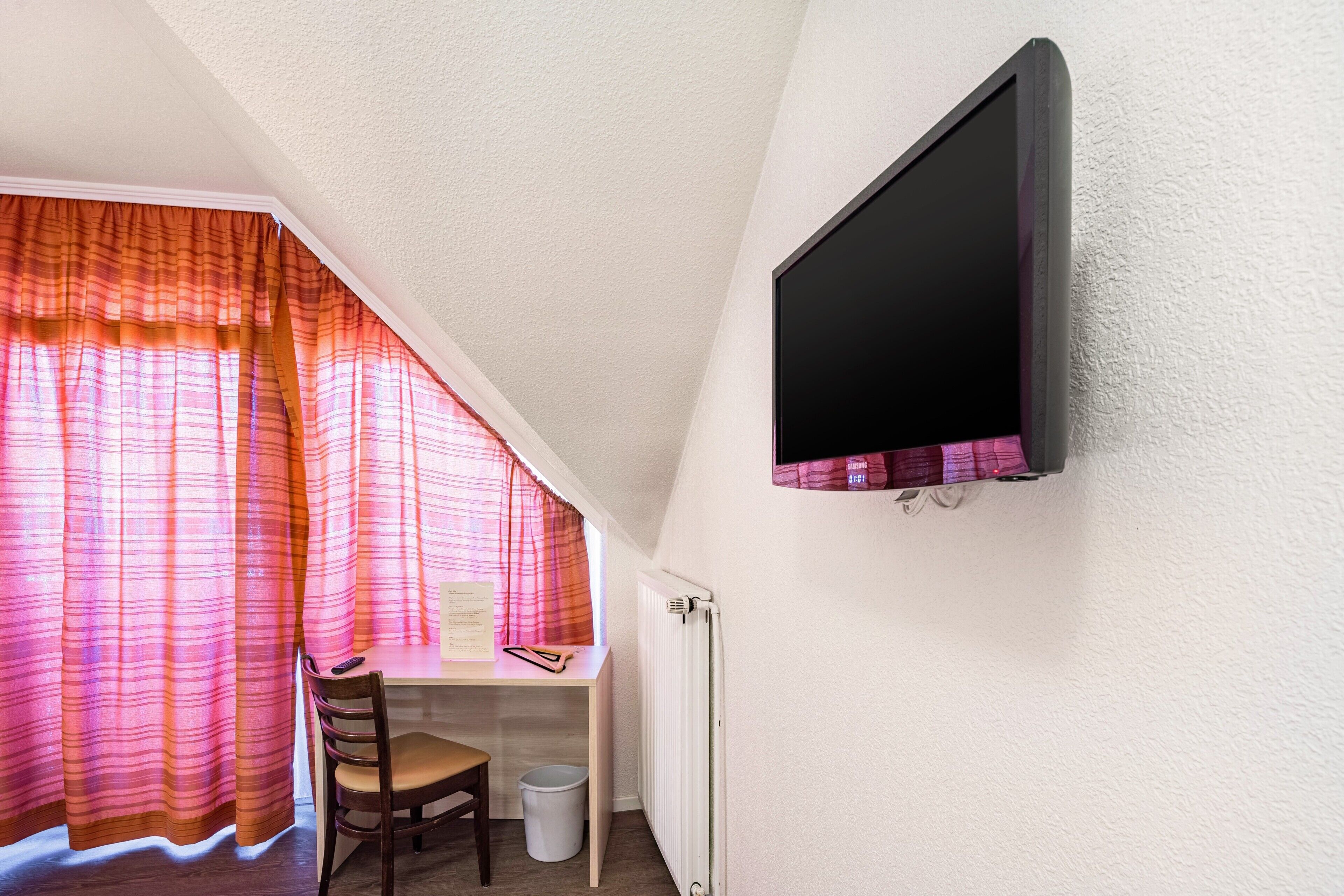 A room with a desk, chair, and a mounted television.