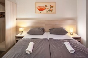 Un lit double avec une literie grise, deux lampes de chevet, une tête de lit en bois et une œuvre d’art encadrée au-dessus du lit.