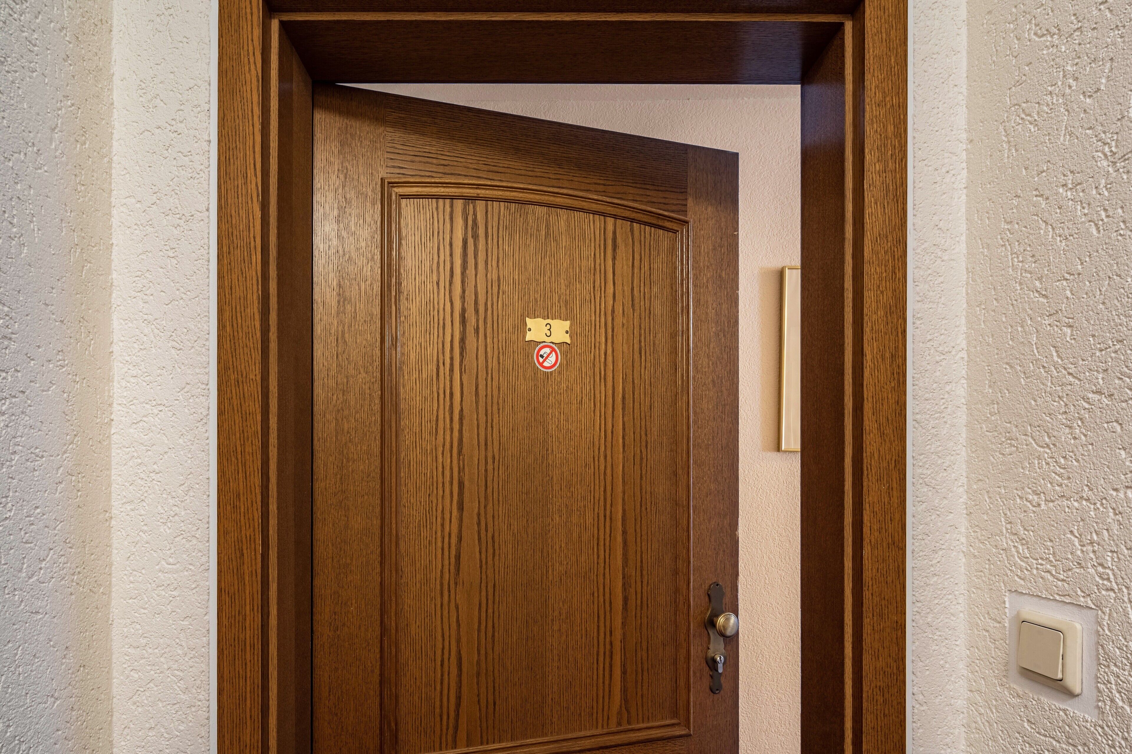 Une porte en bois avec une plaque en laiton portant le numéro « 3 » et un panneau indiquant qu’il est interdit de fumer.