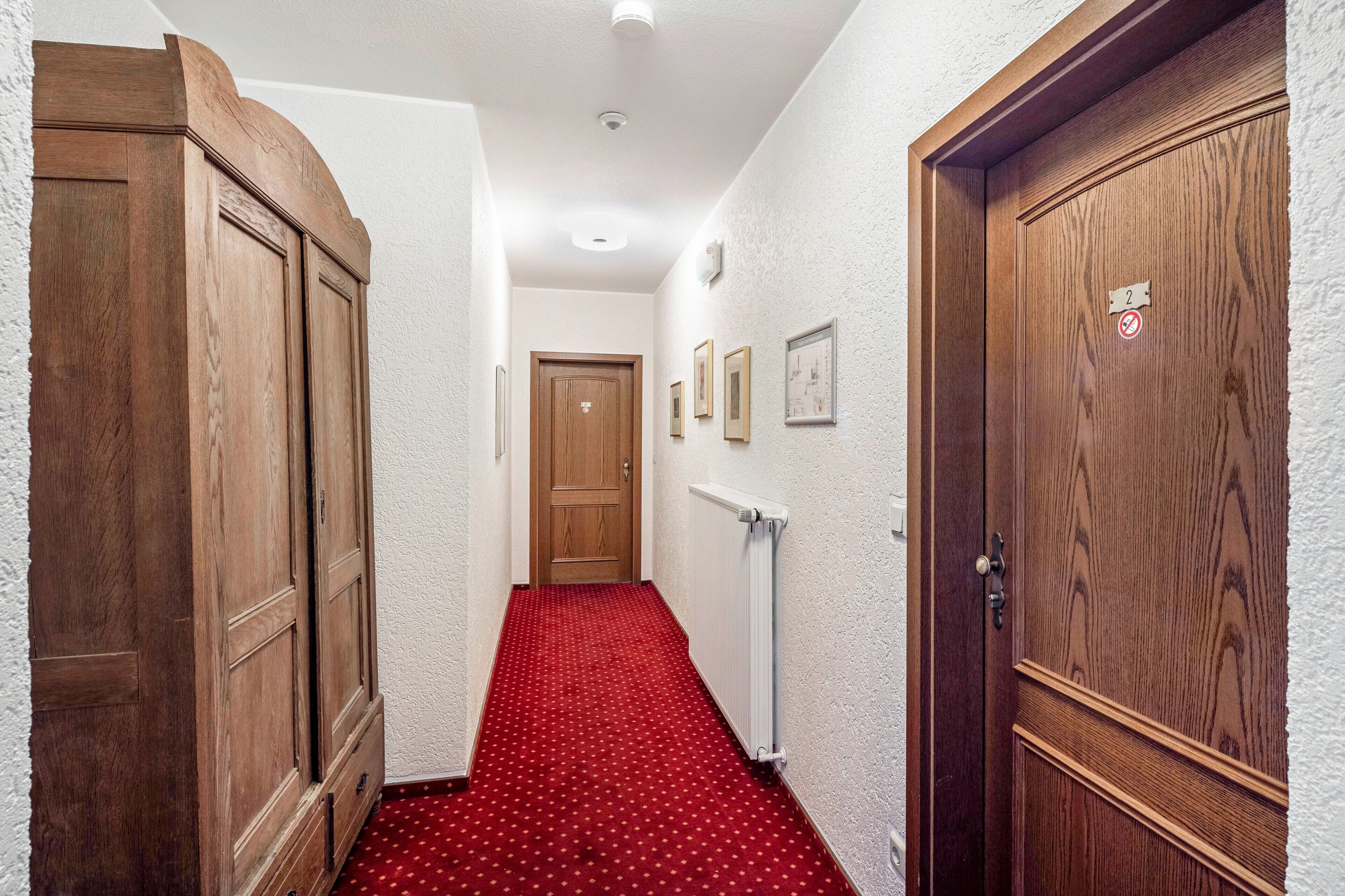Un couloir avec des portes en bois, une moquette rouge et un mur blanc avec un radiateur.