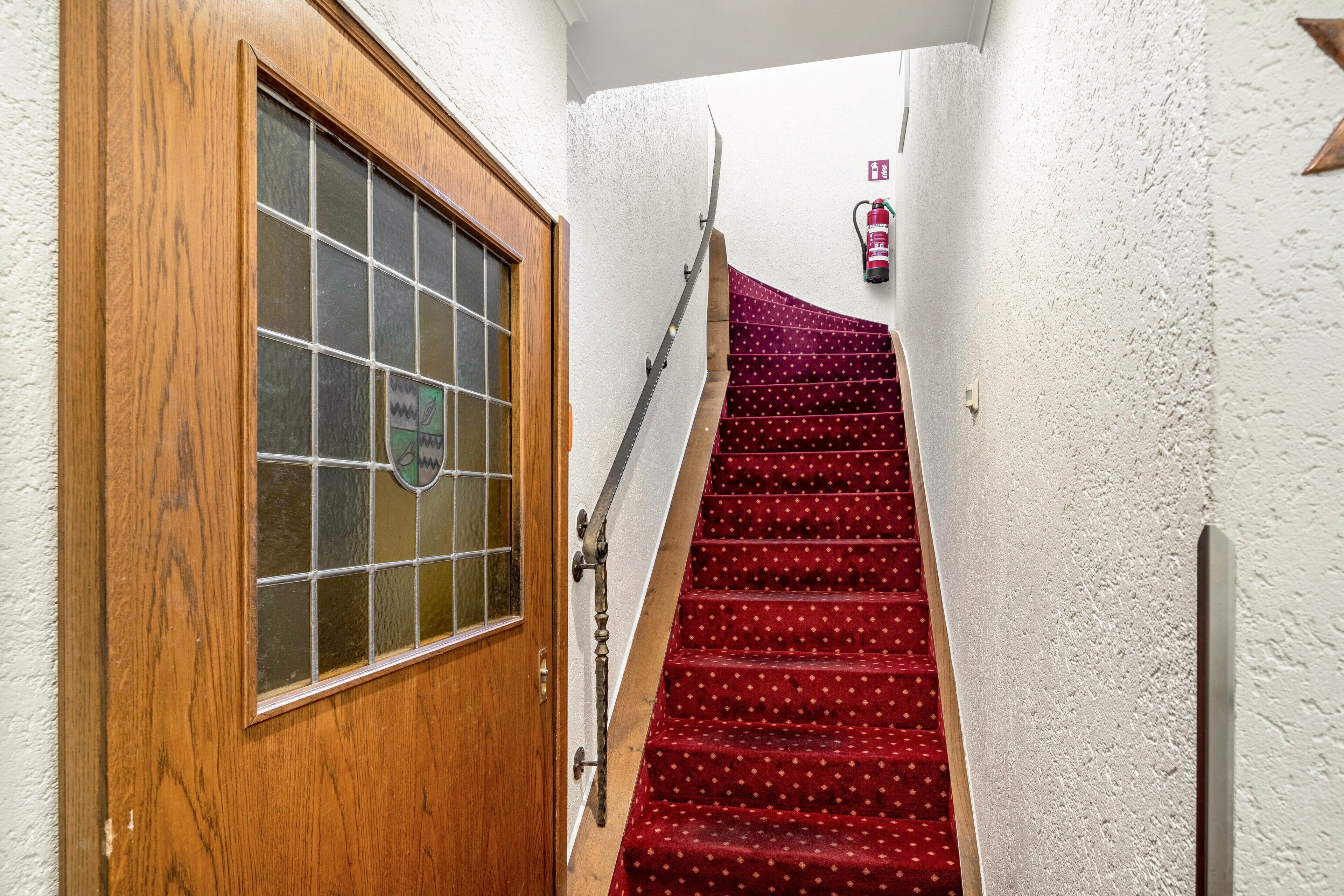 A wooden door with a glass panel, a red carpeted staircase, and a fire extinguisher on the wall.