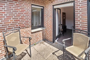 A patio with two wicker chairs, a brick wall, and a sliding glass door leading to an interior space. - Room 'Double Room 4' with Wi-Fi (Rhede)
