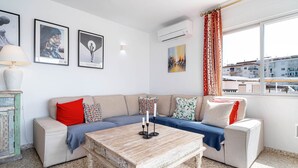 A living room with a sofa, a coffee table, wall art, and an air conditioning unit. - Albaida II 2B Torrecilla Beach Casasol (Nerja)