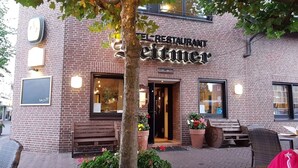 Ein Backsteinhaus mit einem Schild, auf dem 'RESTAURANT Seittimer' steht. Es gibt Außenbereiche mit Sitzgelegenheiten und Blumentöpfen.