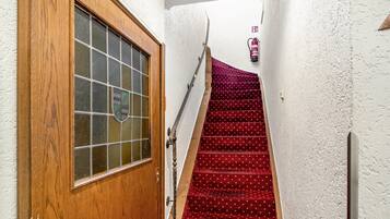 Una puerta de madera con un panel de vidrio, una escalera con alfombra roja y un extintor en la pared.