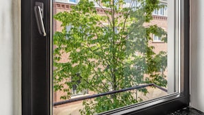 A window with a metal handle, a view of a brick building, and a tree with green leaves.