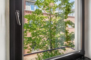 Une fenêtre avec un bouton métallique, une vue sur un bâtiment en briques et un arbre aux feuilles vertes.
