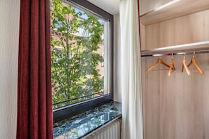 Une pièce avec une fenêtre, un radiateur et une armoire en bois avec des cintres.