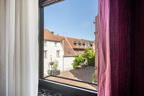 Blick aus dem Fenster auf eine Wohnstraße mit Häusern, einem geparkten Auto und blauem Himmel.