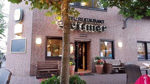 A brick building with a sign reading 'RESTAURANT Seittimer.' There are outdoor seating areas with benches and potted plants.