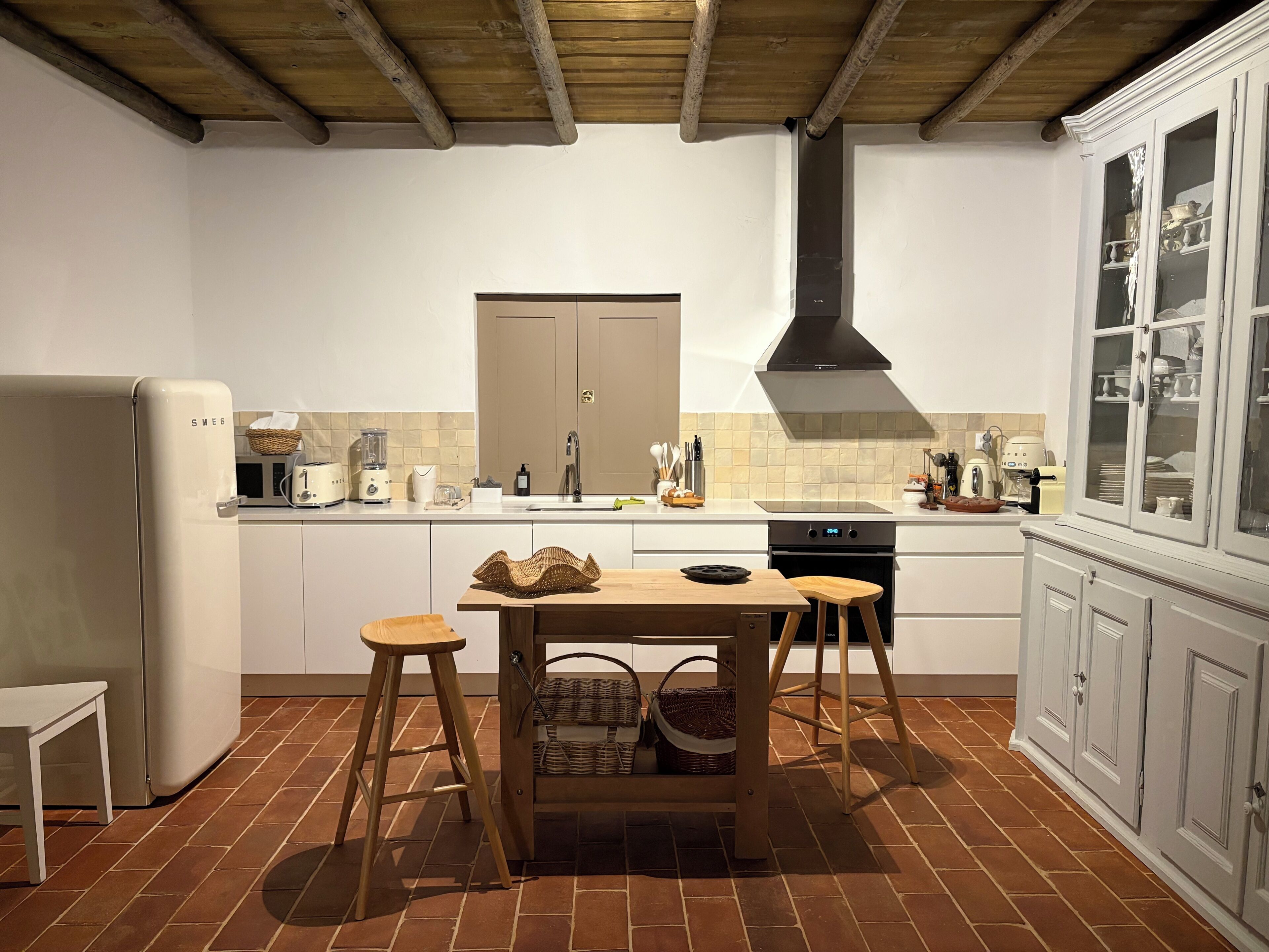 A kitchen with a wooden table, stools, a refrigerator, a stove, and cabinets.