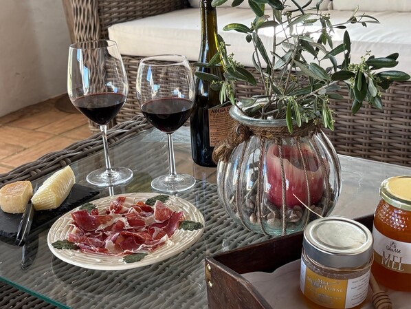 A glass table with a plate of cured meats, two wine glasses, a bottle of olive oil, a potted plant, and jars of honey. - Herdade dos Calvinos Monte 2 (Alandroal)