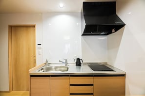 A modern kitchen with a stainless steel sink, a black range hood, and wooden cabinets. - Irodori Hotel KOU (fukuokashi,hakataku,taihakumachi)