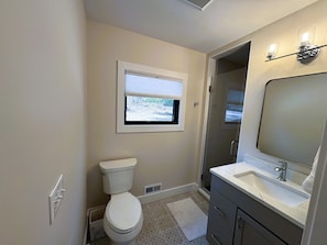 A bathroom with a toilet, a window, a shower, and a sink.