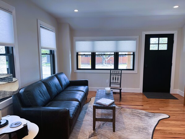 A living room with a black leather sofa, a small wooden table, a chair, and a rug.