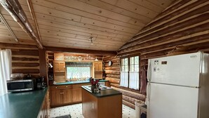 Una cucina in stile baita con pareti in legno, un'isola centrale, un frigorifero e un forno a microonde.
