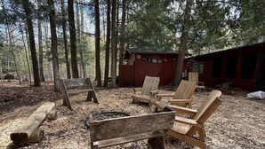 Un rustico chalet con un braciere e sedie di legno immerso in una foresta.