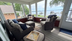 Eine überdachte Veranda mit Korbmöbeln, einer Karte und Blick auf einen See und eine Anlegestelle.