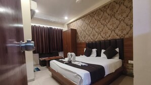 A hotel room with a bed, a wooden wardrobe, a desk, and a window with curtains.