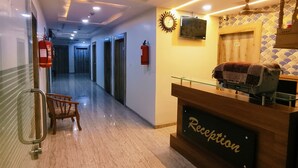 A hotel reception area with a reception desk, a fire extinguisher, a clock, and a television on the wall.