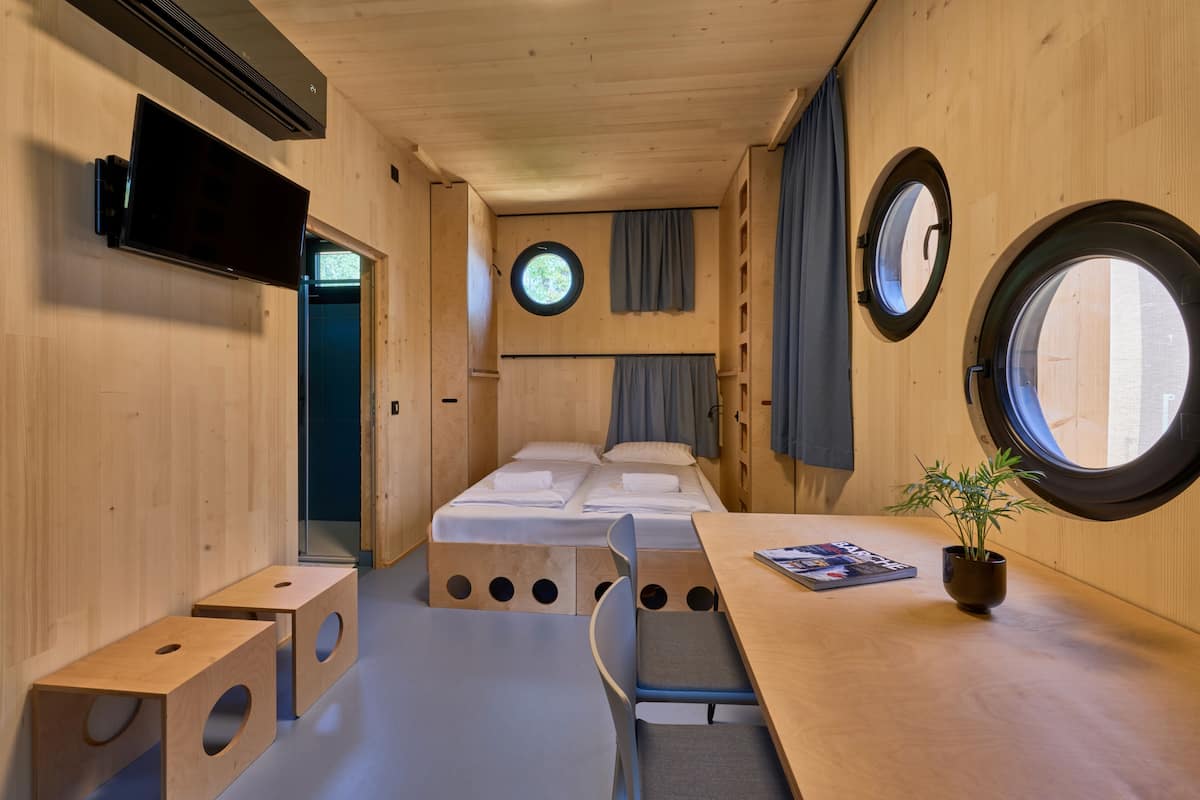 A compact room with a bed, a table, a chair, and a potted plant.