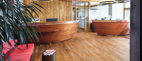 Zona de recepción con mostrador de madera, asientos rojos y una planta.