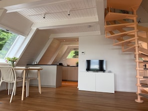 A modern interior with a dining area, kitchen, TV, and a wooden staircase.