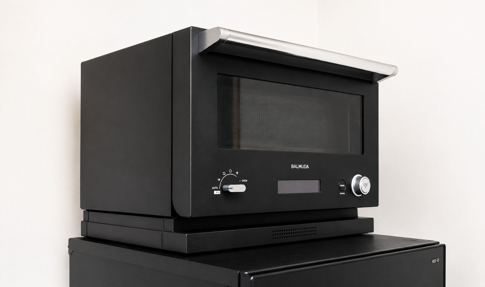 A black electronic device with a display screen, control knobs, and a label 'BALMUDA' on the front.