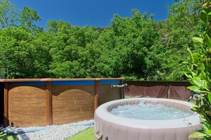Un jacuzzi rodeado por una terraza de madera y un área cercada con árboles al fondo.
